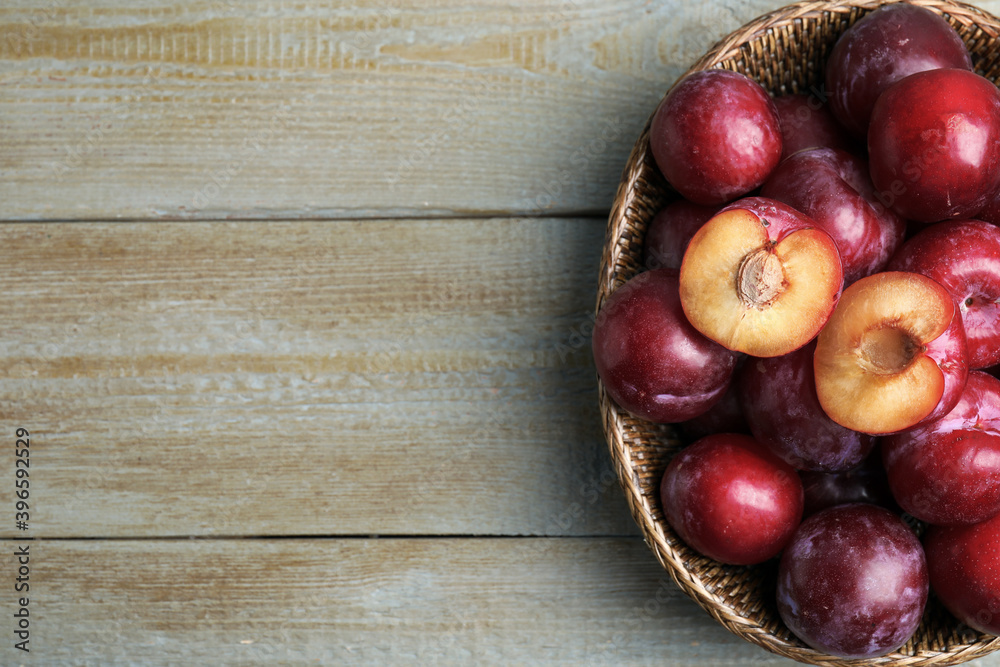 Delicious ripe plums in wicker bowl on wooden table, top view. Space for text Delicious ripe plums in wicker bowl on wooden table, top view. Space for text
