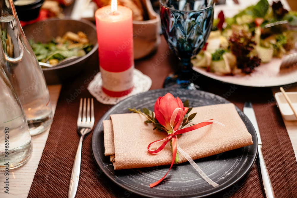 Empty black ceramic plate with a knife, fork on a napkin on a brown background, decorated with a red tulip, close-up. Elegant stylish table setting. Empty black ceramic plate with a knife, fork on a napkin on a brown background, decorated with a red tulip, close-up. Elegant stylish table setting.