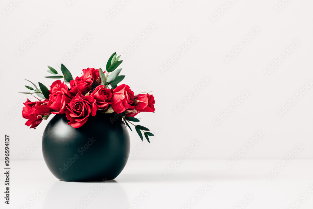 Red roses in black vase on background of white wall. Front view. Stock