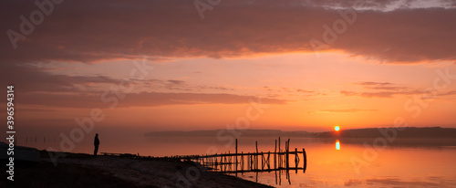 Silhouette of a lonely man standing by the tranqil fjord shore with red sky at sunset. photo