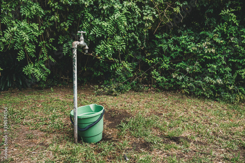 Obraz na płótnie A green bucket next to a tap in a garden w salonie