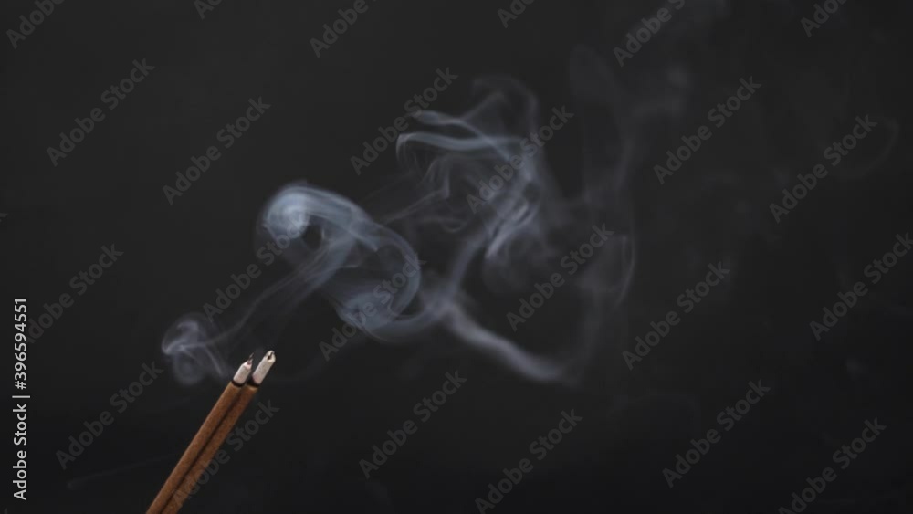 Slow motion shot of Incense Stick emitting smoke against the black background Slow motion shot of Incense Stick emitting smoke against the black background