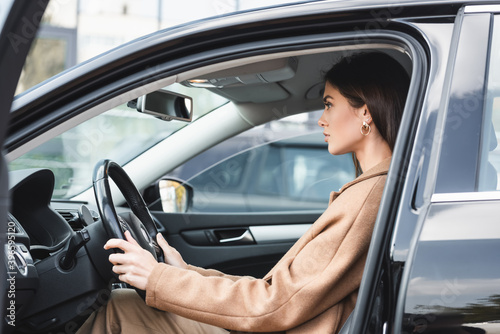  woman in trench coat sitting in car with open door and holding steering wheel © LIGHTFIELD STUDIOS
