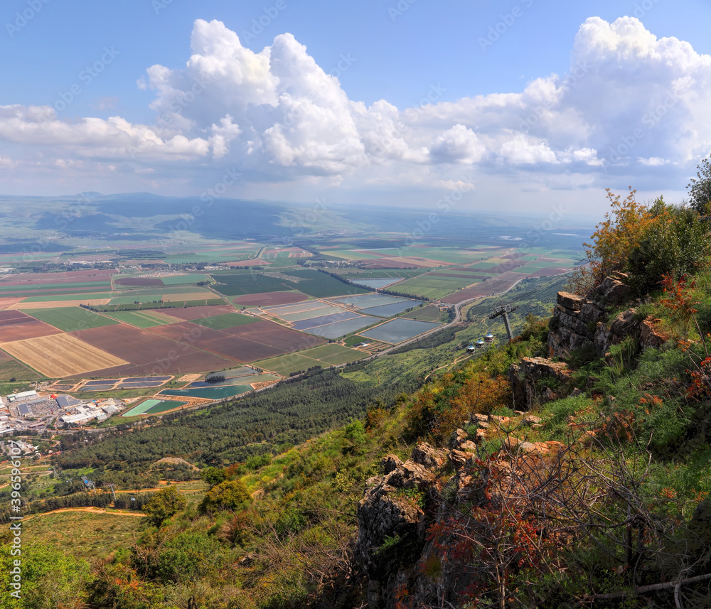 Obraz premium Panoramic view from Manara Cliff on Hula Valley. Kiryat Shmona city and beautiful farming landscape with agricultural land. Cableway cabins go up to the mountain. Upper Galilee. Northern Israel