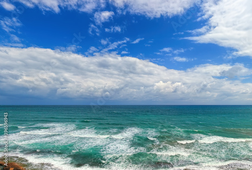 Magnificent sea panoramic landscape. White foaming waves surf. Stony seashore. Seascape with impressive blue sky and white bizarre clouds