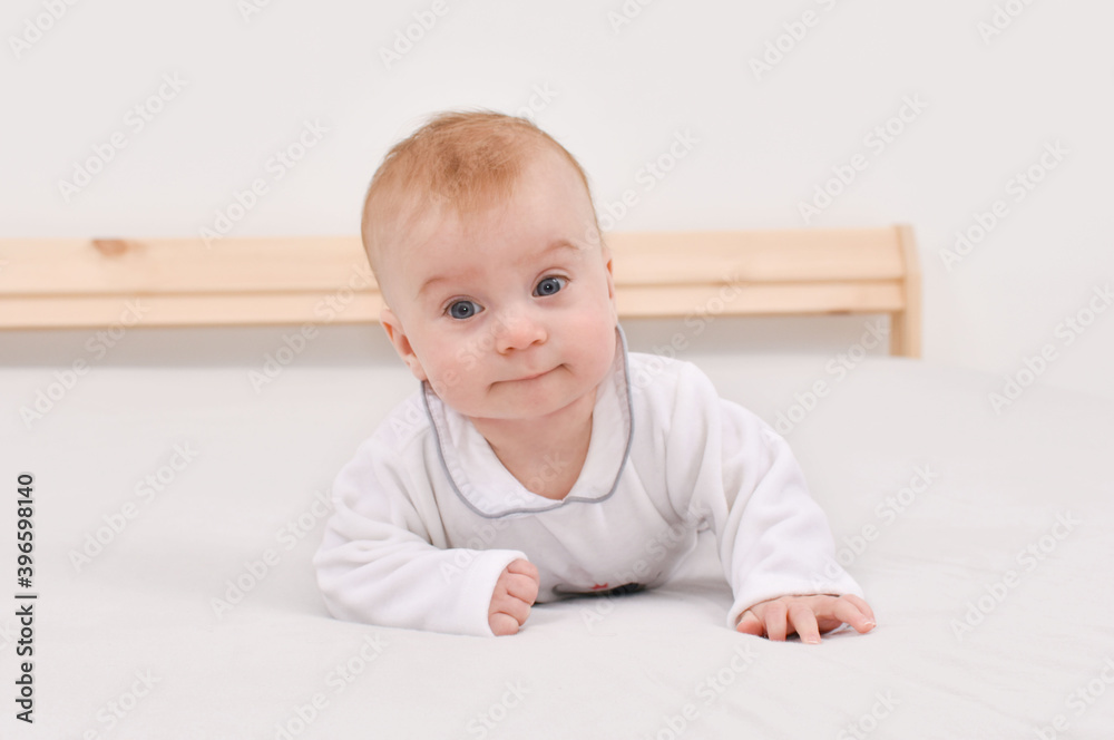 Adorable happy caucasian four-five months baby lying on stomach on bed, looking at camera Adorable happy caucasian four-five months baby lying on stomach on bed, looking at camera