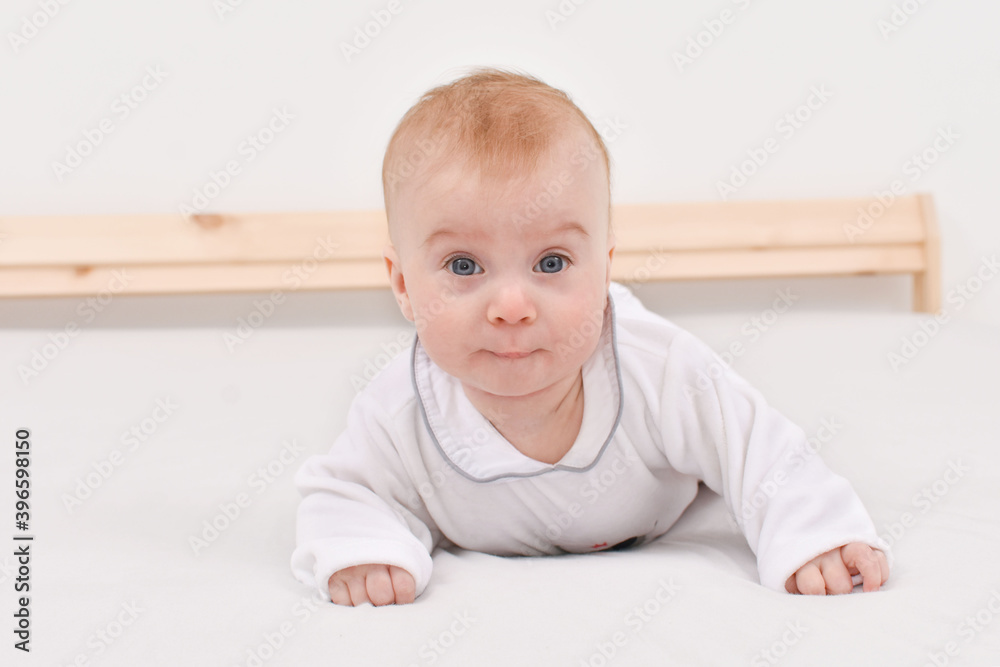 Adorable happy caucasian four-five months baby lying on stomach on bed, looking at camera Adorable happy caucasian four-five months baby lying on stomach on bed, looking at camera