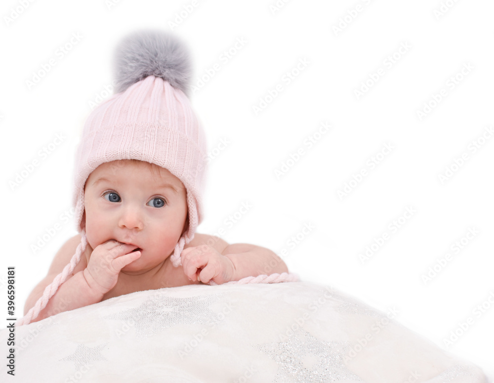 Thoughtful, adorable happy caucasian four-five months baby in winter knitted hat lying on bed, biting finger, isolated on white. Baby care and winter clothes concept. Copy space. Thoughtful, adorable happy caucasian four-five months baby in winter knitted hat lying on bed, biting finger, isolated on white. Baby care and winter clothes concept. Copy space.