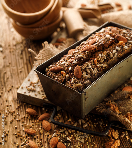 Bild auf Leinwand Homemade buckwheat bread with the addition of nuts and seeds in a baking tin on a wooden table, close up view