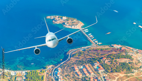 White passenger jet plane in the sky - Aircraft flies high over the city and sea coast of Kusadasi port and island - Kusadasi, Izmir