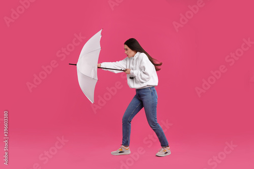 Fotografie Woman with white umbrella caught in gust of wind on pink background
