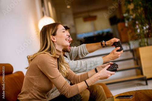 Young couple playing video games at home, sitting on sofa and enjoying themselves