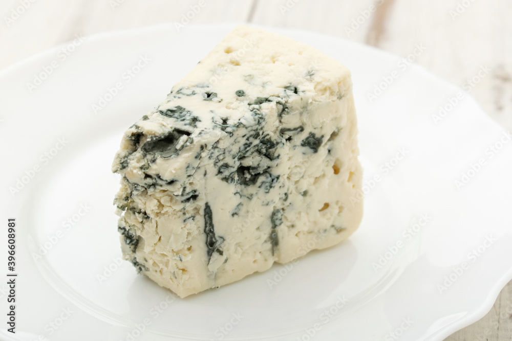 Blue cheese on a white plate on a wooden background.