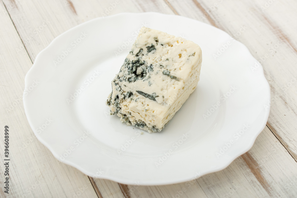 Blue cheese on a white plate on a wooden background.