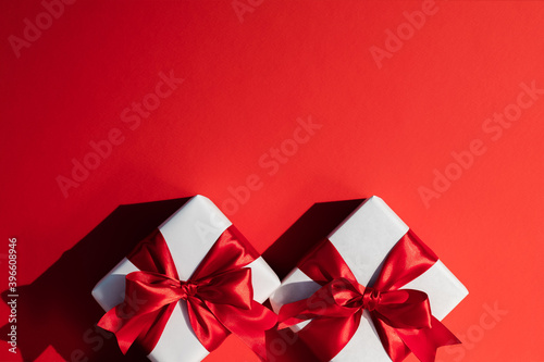 Romantic present. Valentine Day. Couple of white wrapped gift boxes with ribbon bows isolated on red copy space festive background. Greeting card. Holiday decorative composition.