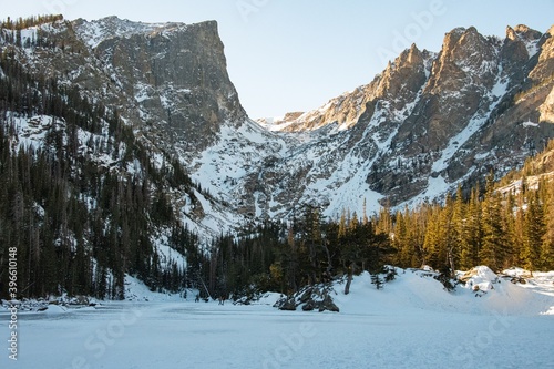 Fototapeta Naklejka Na Ścianę i Meble -  A view of Dream Lake in Rocky Mountain National Park with snow covered peaks surrounded by a forest of trees, snow, and ice.