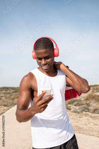Smiley young black sportsman with headphones who listens to music with his mobile. Concept of technology.