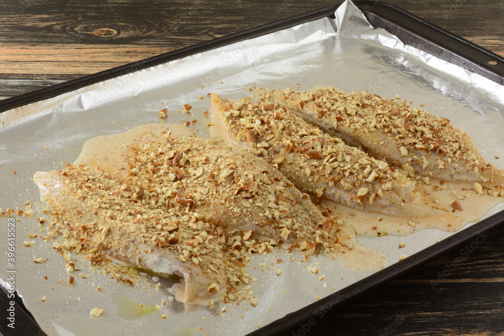 Fresh raw tilapia fish fillets dipped in light tempura batter with pretzel crumb crust on aluminum foil on baking sheet Fresh raw tilapia fish fillets dipped in light tempura batter with pretzel crumb crust on aluminum foil on baking sheet