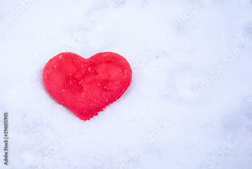 Red plush heart, lying in winter on the white pure snow in the sun. Love the concept of Valentine's Day. Lost heart top view. Valentine's day background with space to copy.