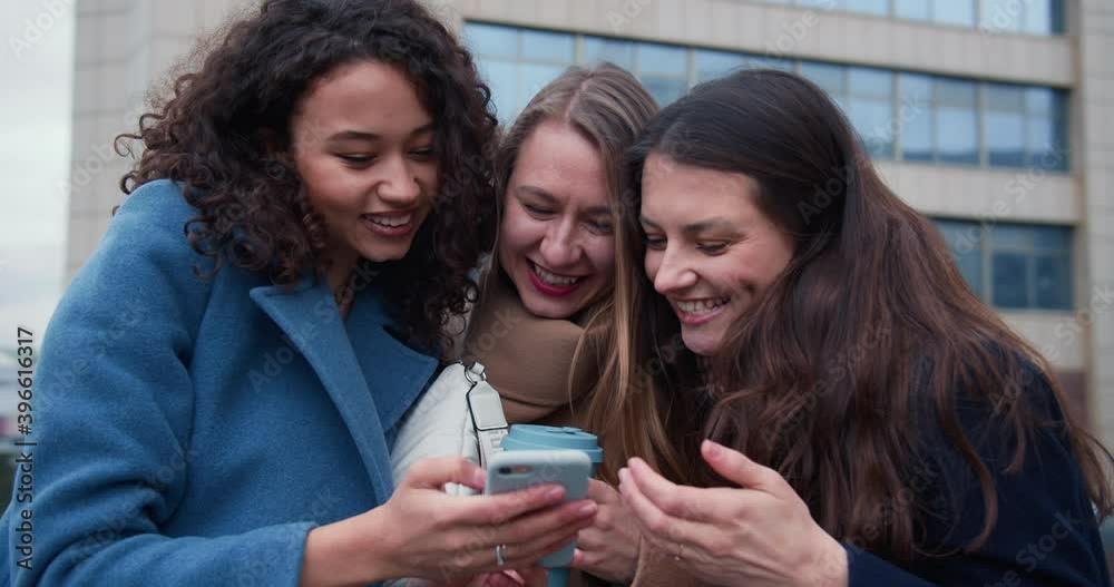 Social networks concept. Three beautiful young happy women using internet on smart phone in city street on autumn day. Social networks concept. Three beautiful young happy women using internet on smart phone in city street on autumn day.