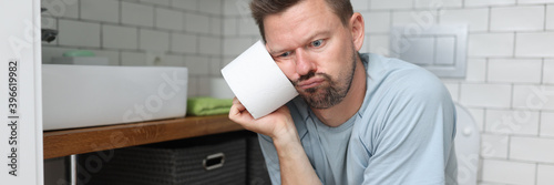 Canvas Print Pensive man sits on toilet with a roll of toilet paper