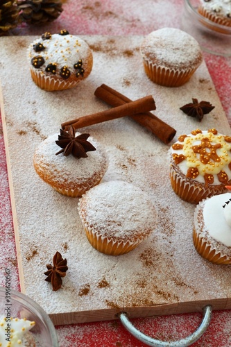 Christmas composition: Christmas cupcakes decorated with icing and surrounded by cinnamon sticks and star anise on a background of powdered sugar