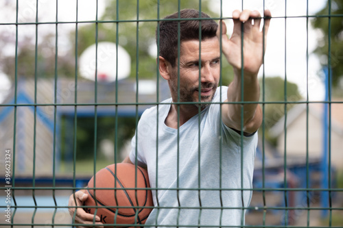 athlete stands with basketball ball looks through the fence