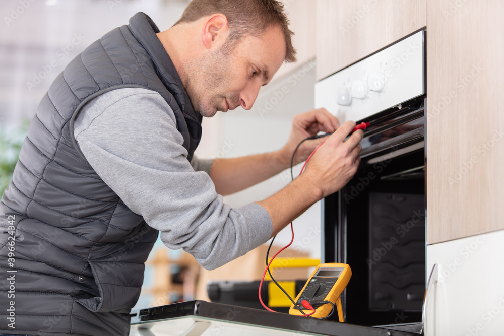 young male technician checking oven with digital multimeter young male technician checking oven with digital multimeter