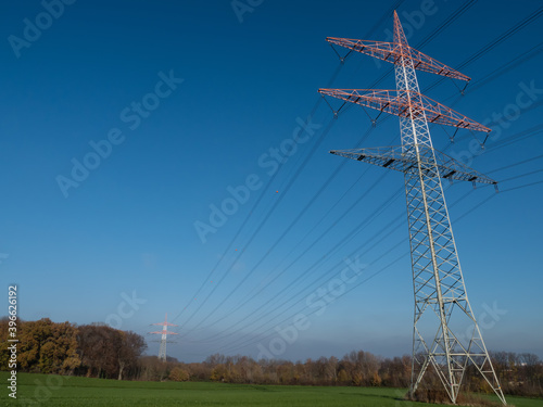 Freileitungsmast vor blauem Himmel auf einer grünen Wiese im Spätherbst photo