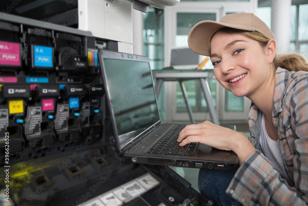 woman using a laptop while maintaining a photocopier woman using a laptop while maintaining a photocopier