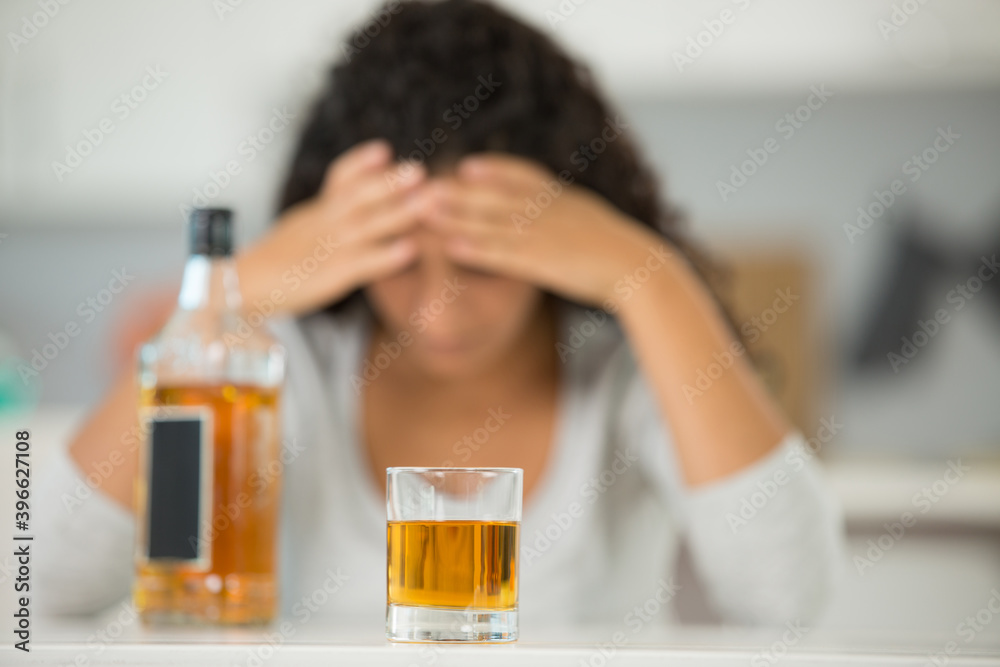 woman with head in her hands alcoholic drink in foreground woman with head in her hands alcoholic drink in foreground