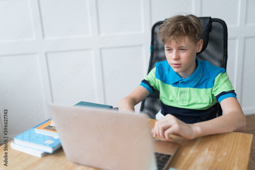 Good-looking European boy is playing computer games on his laptop with enthusiasm. He's wearing a trendy stripy polo shirt Good-looking European boy is playing computer games on his laptop with enthusiasm. He's wearing a trendy stripy polo shirt