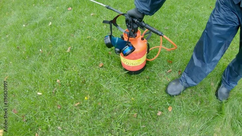 Lawn treatment with insecticides and toxins from ixodic mites and other blood sucking parasites. A man in a protective suit sprays poison on the grass
