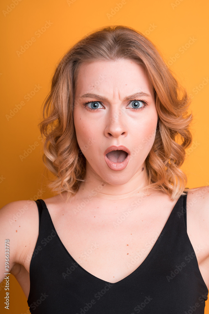 Naklejka premium Portrait of an upset young blonde Caucasian girl with her mouth wide open. Isolated on orange background. Feelings and emotions