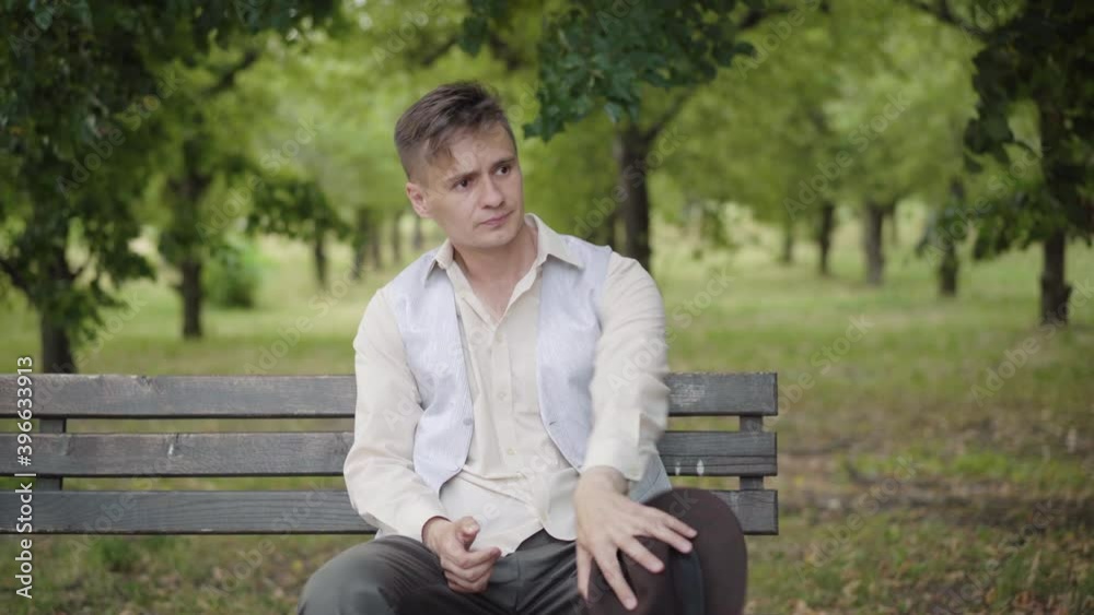 Unhappy nervous elegant man sitting on bench in summer park and looking around. Portrait of young stressed Caucasian guy having problems thinking outdoors. Stress and troubles. Unhappy nervous elegant man sitting on bench in summer park and looking around. Portrait of young stressed Caucasian guy having problems thinking outdoors. Stress and troubles.