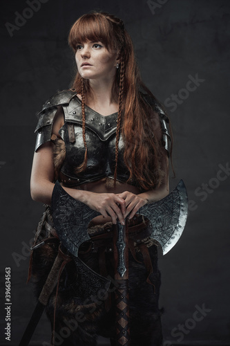 Beautiful northern amazon in dark armour with huge axe posing in dark background.