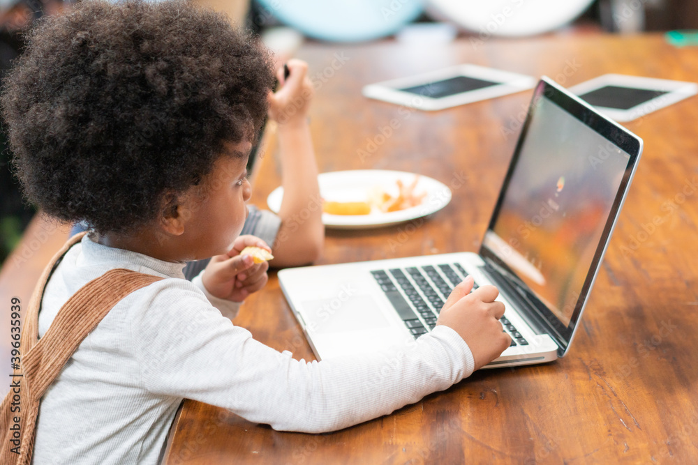 Little black boy enjoy learning and playing with laptop computer in the restaurant. Kid education and lifestyle concept Little black boy enjoy learning and playing with laptop computer in the restaurant. Kid education and lifestyle concept