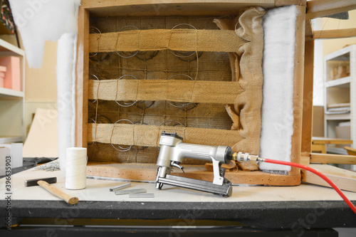 Inside upholstery workshop. Old chair from 50s renovation. Upholstery tools on table. Repairing old furniture. Wooden construction with springs and straps.