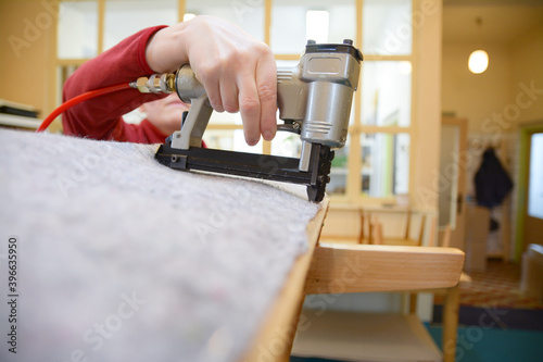 Hand working with pneumatic stapler. Old armchair restoring. Nonwoven upholstery material. Woman hand work in upholstery workshop. photo