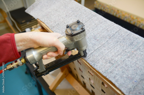 Hand working with pneumatic stapler. Old armchair restoring. Nonwoven upholstery material. Woman hand work in upholstery workshop.