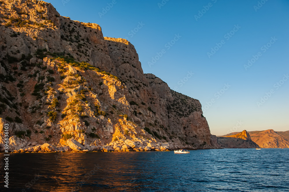 pleasure boat with tourists in the sea against the backdrop of rocks at sunset.