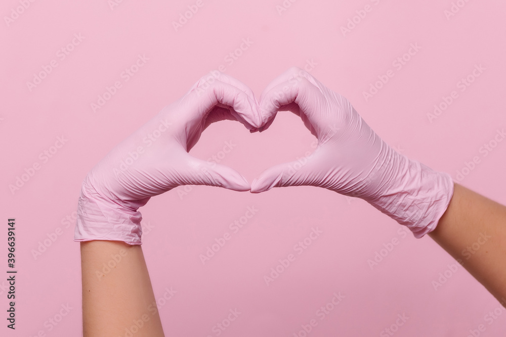Hands heart sign in medical protective latex gloves. Professional beauty salon.  Coronavirus covid-19. Hygiene.   pink background place for text copyspace one color monochrome. positive hope