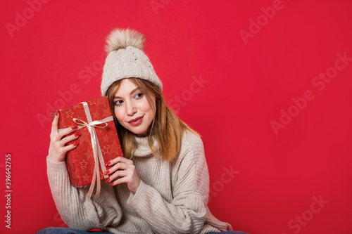 Dreaming winter girl holding christmas present on red background