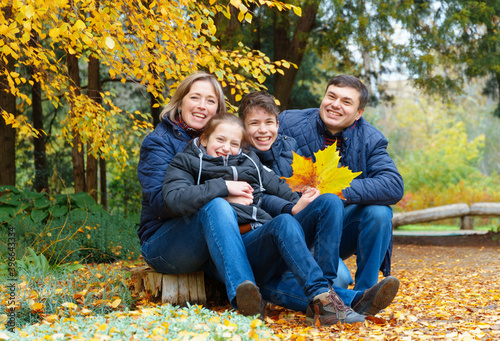 family relaxing outdoor in autumn city park, happy people together, parents and children, they talking and smiling, posing near yellow birch leaves, beautiful nature