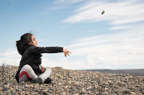 pequeña niña sentada en piedras con abrigo y pelo recogido photo