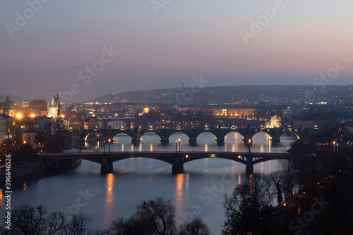 view of the Vltava river and the bridges on it between the bridges and the Charles Bridge and the surrounding architecture and light from the street lights in the center of Prague after sunset