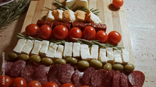 Flat lay of cheese and meat platter. Slices of cheese, smoked sausage, tomatoes, olives and rozmarin arranged in a shape of Christmas Tree. Food for Christmas holiday. Slowmotion photo