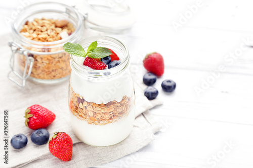 Tasty granola with cream and berries on white wooden background