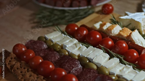 Flat lay of cheese and meat platter. Slices of cheese, smoked sausage, tomatoes, olives and rozmarin arranged in a shape of Christmas Tree. Food for Christmas holiday. Slowmotion photo