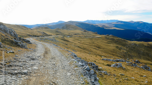 A gravel road winding along the high altitude pastures in Latorita Mountains. Autumn season with its yellowish colored grass.